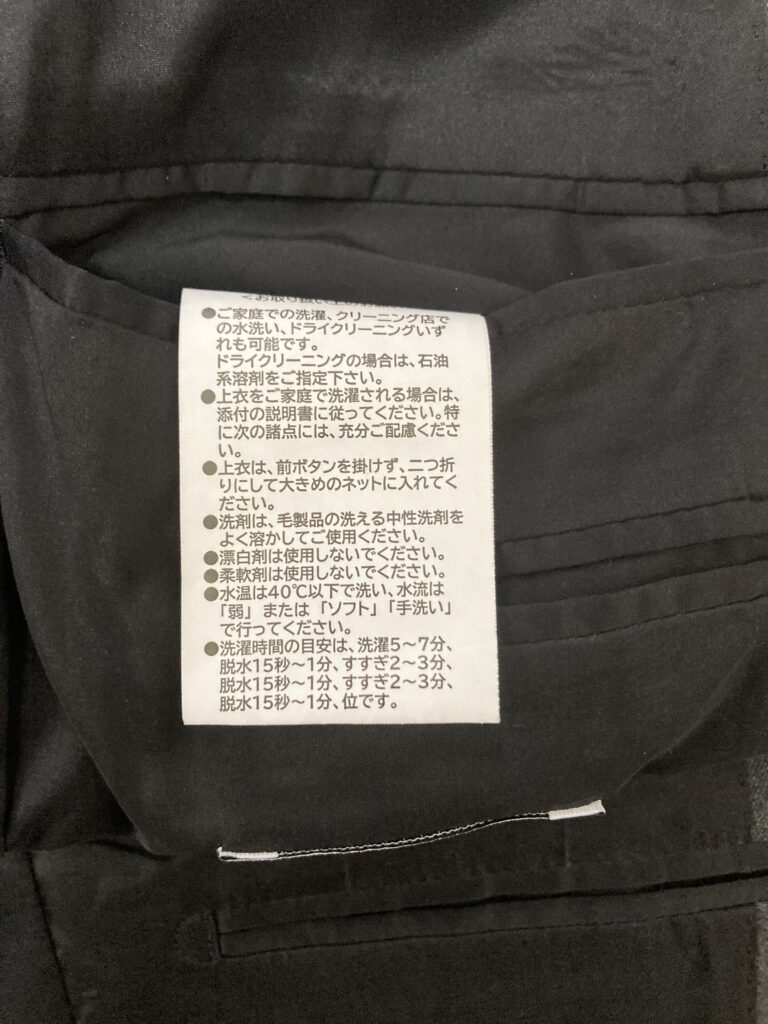 スーツの内ポケットに縫い付けられている家庭での洗い方が詳しく記載された白い品質表示タグ